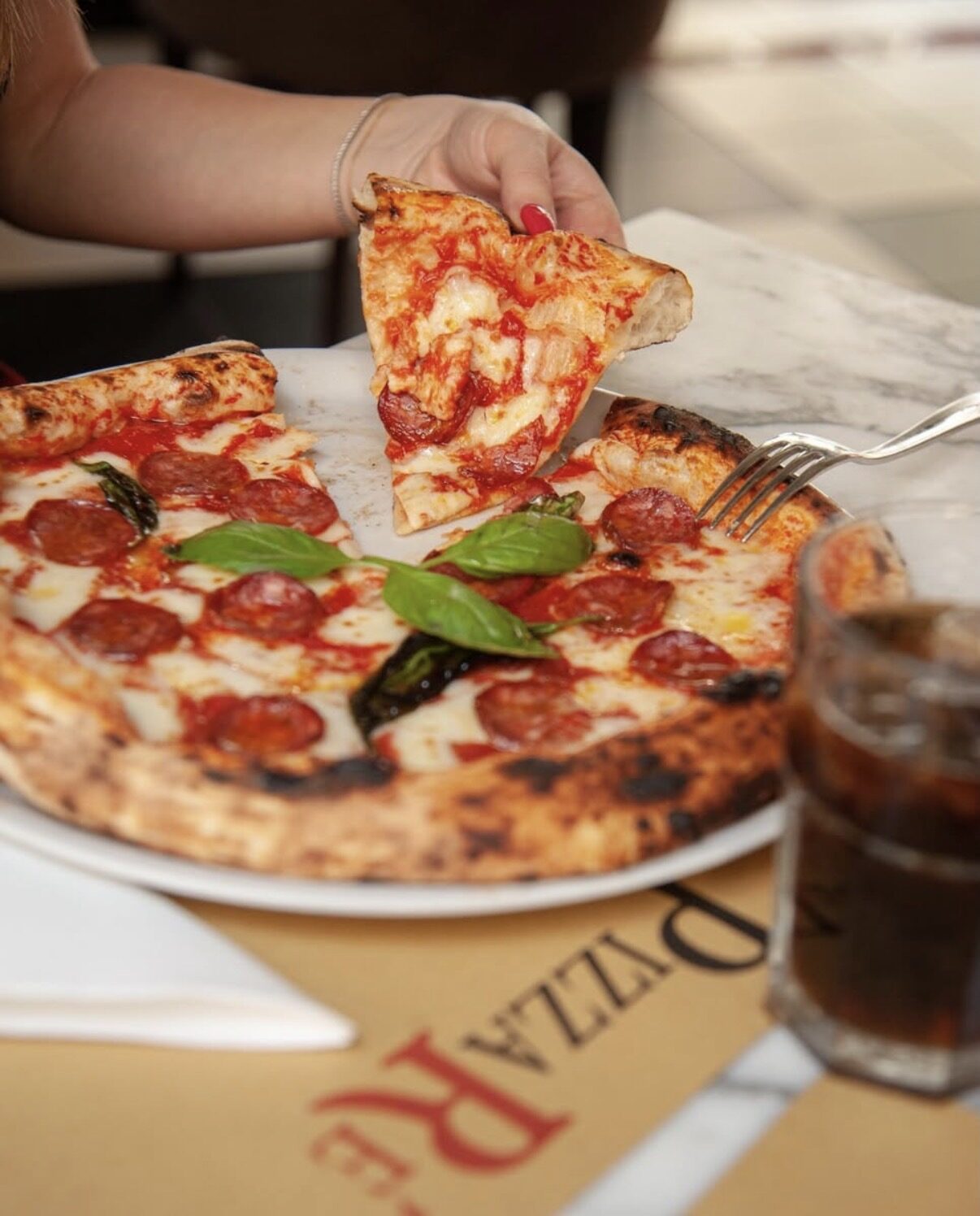 Trancio di pizza diavola sollevato dal tavolo di marmo di PizzaRé