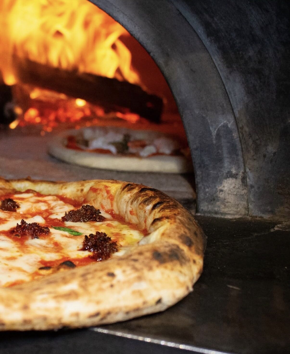 Pizza appena sfornata davanti alla bocca del forno a legna acceso