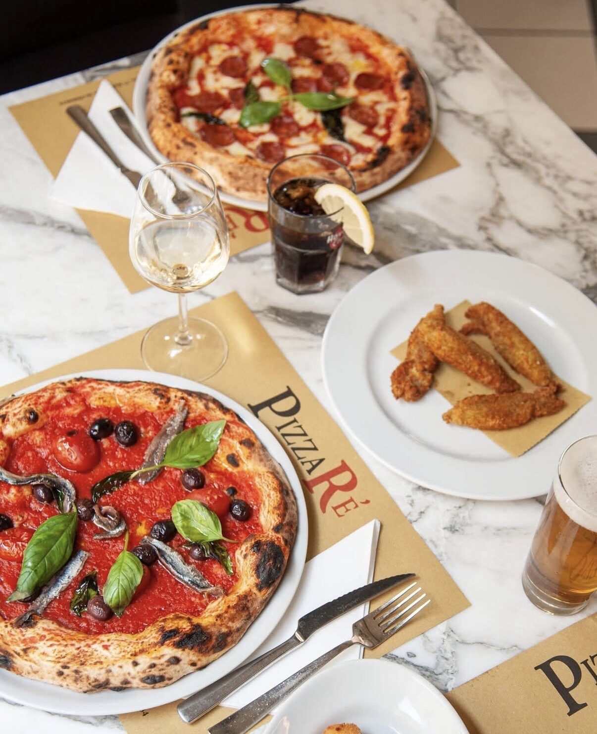 Tavolo di marmo con due pizze, fritti e tovagliette PizzaRé