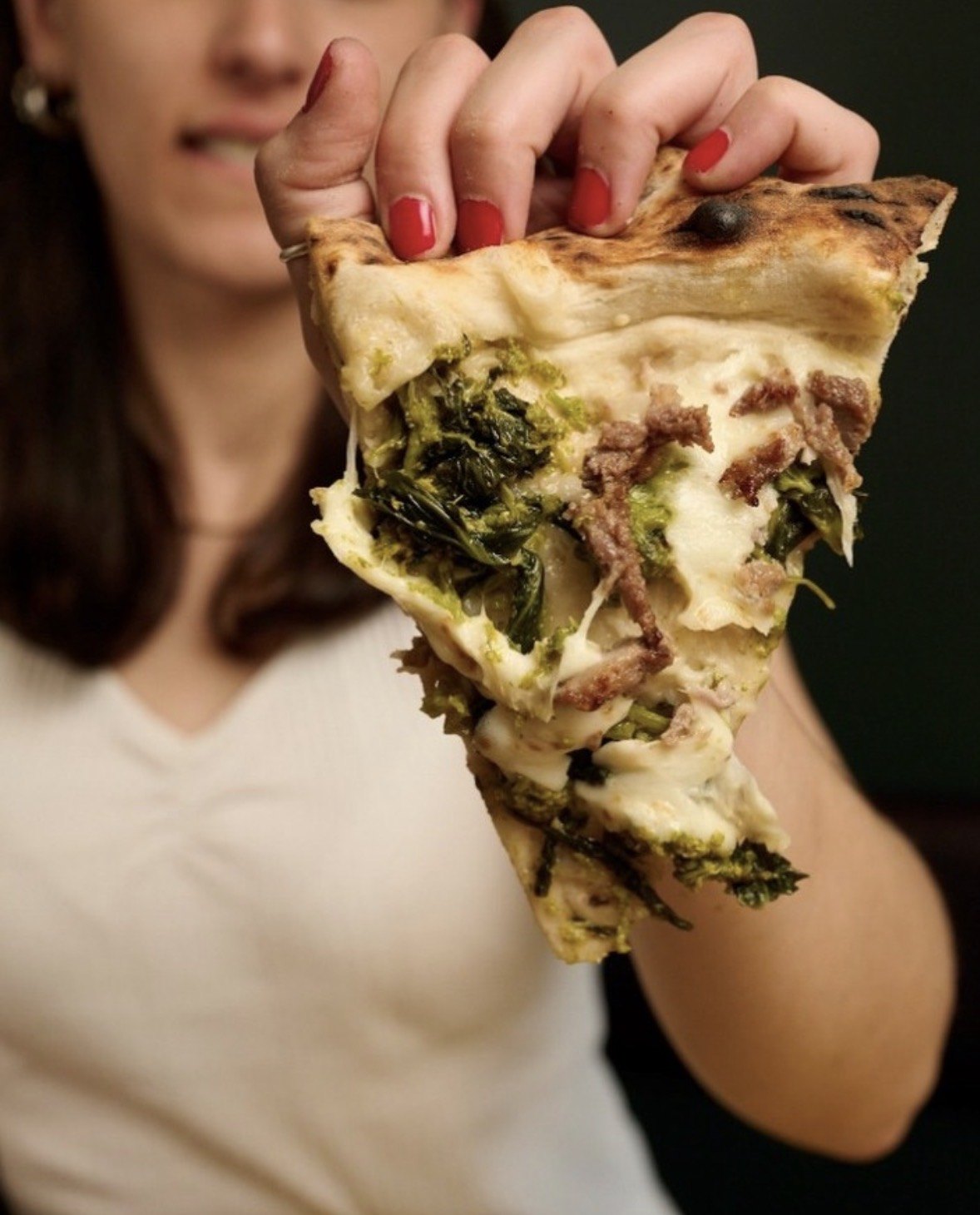 Ragazza che tiene una fetta di pizza bianca con salsiccia e friarielli
